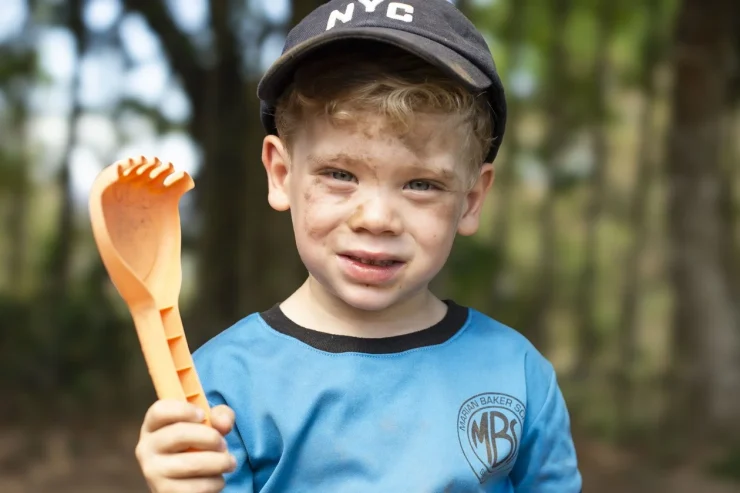 MBS early childhood student outdoors holding a garden tool in his school shirt